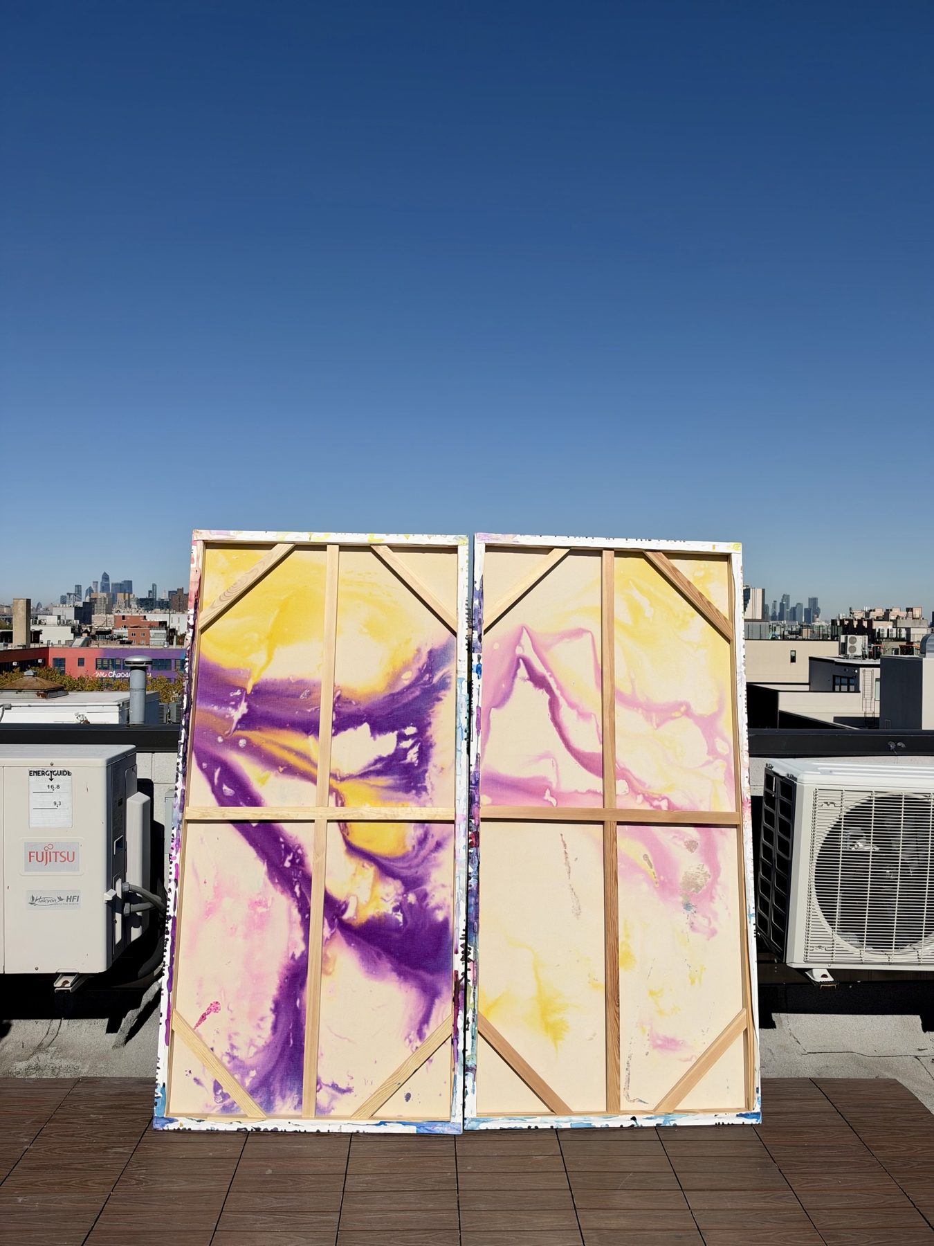The backs of both canvases, showing purple and yellow paint that has bled through the raw canvas around the wooden stretcher bars.