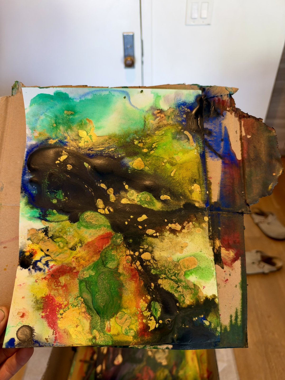 A test on paper held over cardboard, green and yellow washes with a black pour and gold spatter.